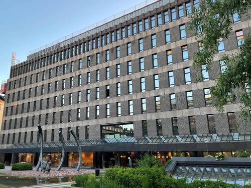 Utsikt mot en stor tegelbyggnad med växter och en lampa i förgrunden.